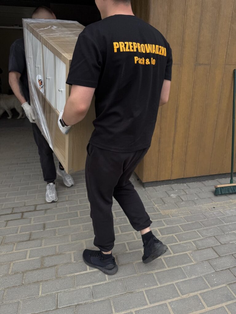 Dwóch pracowników firmy przeprowadzkowej Go Przeprowadzki wnosi zabezpieczony mebel do domu klienta – Warszawa, czerwiec 2025, przeprowadzka z Bemowa na Białołękę