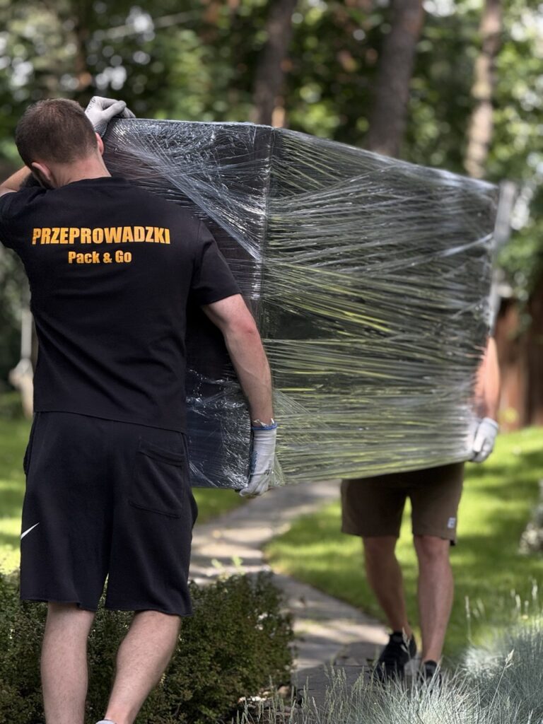 Dwóch pracowników niesie zabezpieczoną folią komodę – transport mebli Warszawa